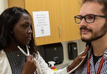 Nusing student in medical coat with stethoscope, listening to the breathing of a patient